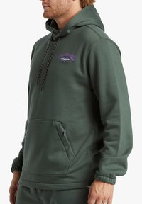 Felpa verde realizzata in morbido tessuto. Dotata di tasca frontale, cappuccio con cordino regolabile e dettagli del logo viola. Maniche con polsini.