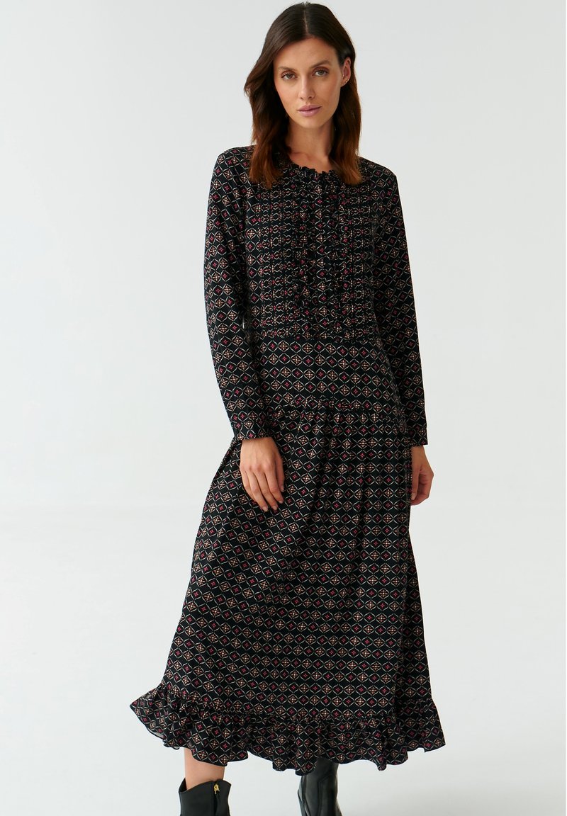 Długa czarna sukienka z geometrycznym wzorem w czerwono-białe kolory, z falbankowym dekoltem i dołem, długimi rękawami oraz warstwowym fasonem.