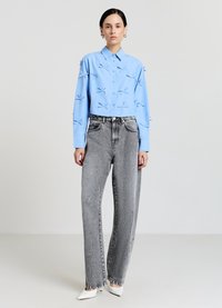 Chemise en coton bleu clair avec boutons sur le devant et accents 3D décoratifs ; associée à un jean large taille haute gris et des talons blancs.