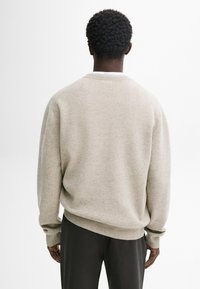 Pull beige clair avec une finition texturée, doté d'un col et de poignets côtelés, accompagné d'un pantalon foncé à coupe décontractée.