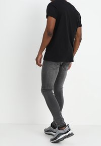 Camiseta negra de manga corta, jeans ajustados grises y zapatillas negras/grises. Tejido suave y detalles mínimos; los jeans tienen bolsillos traseros.