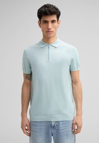 Jasnoniebieska koszulka polo z krótkim rękawem i zamkiem błyskawicznym przy kołnierzyku, wykonana z gładkiego, lekkiego materiału. Charakteryzuje się regularnym krojem i subtelną fakturą.