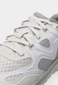 Κοντινή λήψη από λευκό και γκρι αθλητικό παπούτσι με υφασμάτινη διχτυωτή επιφάνεια, συνθετικές επικαλύψεις και λευκά κορδόνια δεμένα πάνω σε επενδεδυμένη γλώσσα.