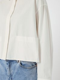 White long-sleeve shirt with a large front pocket worn over blue denim jeans, focusing on the torso and waist area.