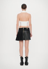 Black leather pleated skirt with a zippered back, paired with a strapless white top. Smooth texture, fitted design, and short length.
