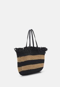 Torebka na ramię z plecionych włókien w czarno-beżowe paski, czarnymi skórzanymi uchwytami oraz frędzlami wzdłuż górnej krawędzi, stojąca na białym tle.