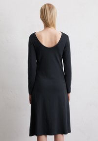 Schwarzes, langärmliges Kleid mit rundem Rückenausschnitt und ausgestelltem Saum, aus glattem Stoff gefertigt, bietet einen lockeren Sitz und ein einfaches Design.