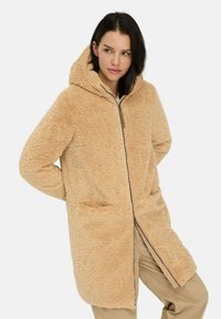 Beige fleece-gevoerde jas met een capuchon, voorzien van een volledige rits, zijzakken en een zachte, gestructureerde afwerking. Casual ontwerp voor warmte.