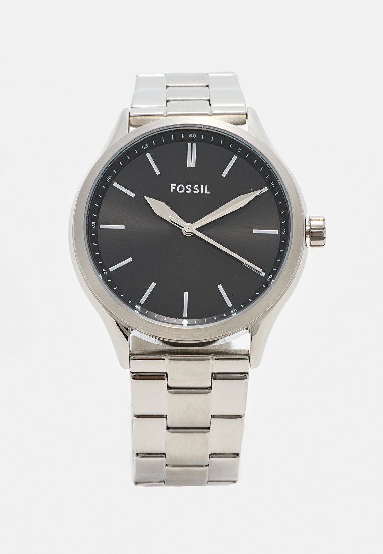 Montre Fossil avec un bracelet en acier inoxydable argenté, un cadran analogique noir, des index horaires en ton argenté, et un boîtier rond avec une couronne sur le côté.