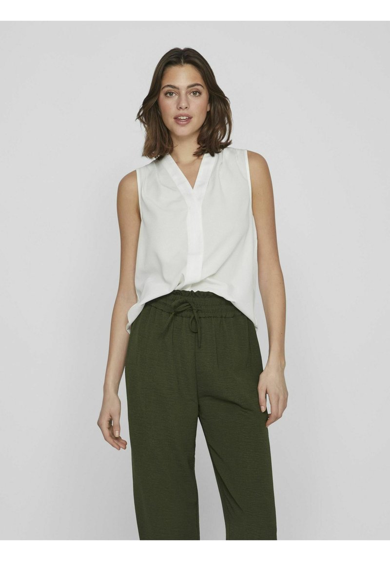 Blouse blanche sans manches avec un col en V et une patte de boutonnage à l'avant, associée à un pantalon olive décontracté avec une taille élastique.
