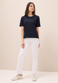 Camiseta de manga corta azul marino con el texto "ETERNAL" en un tono más claro, combinada con pantalones rectos blancos y zapatillas ligeras.