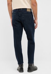 Granatowe dżinsy o wąskim kroju, z pięcioma kieszeniami i subtelnym przeszyciem. Posiadają skórzaną naszywkę z logo na tylnej części pasa.