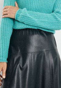 Maglione lavorato a maglia turchese con texture a coste abbinato a una gonna nera in finta pelle con vita elastica liscia e dettagli a pieghe.