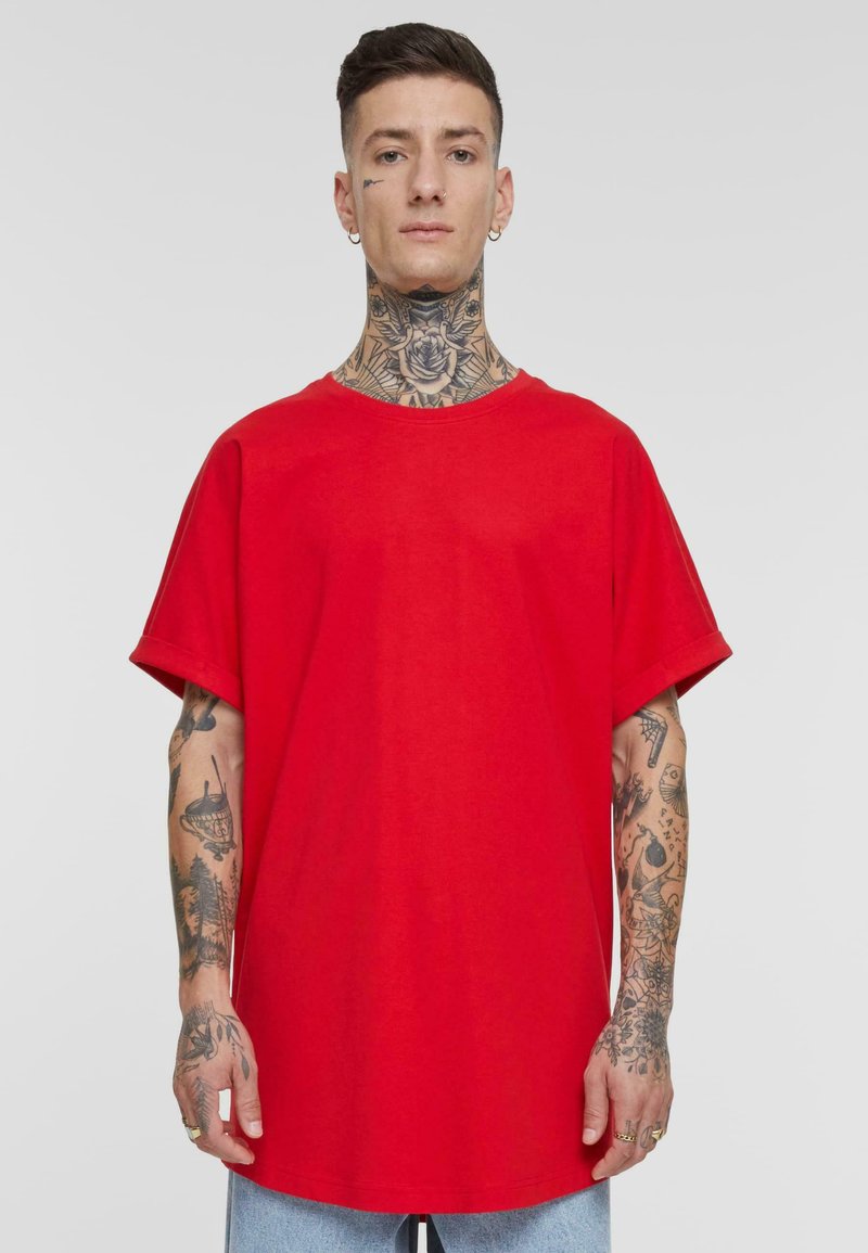 Camiseta de algodón roja con diseño oversize, mangas cortas y cuello redondo. Presenta tatuajes visibles en los brazos.