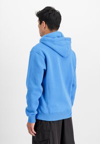 Modra kapuca s puloverjem z teksturirano tkanino, rebrastimi manšetami in robom. Zadnja stran ima preprost dizajn brez logotipov ali vzorcev.