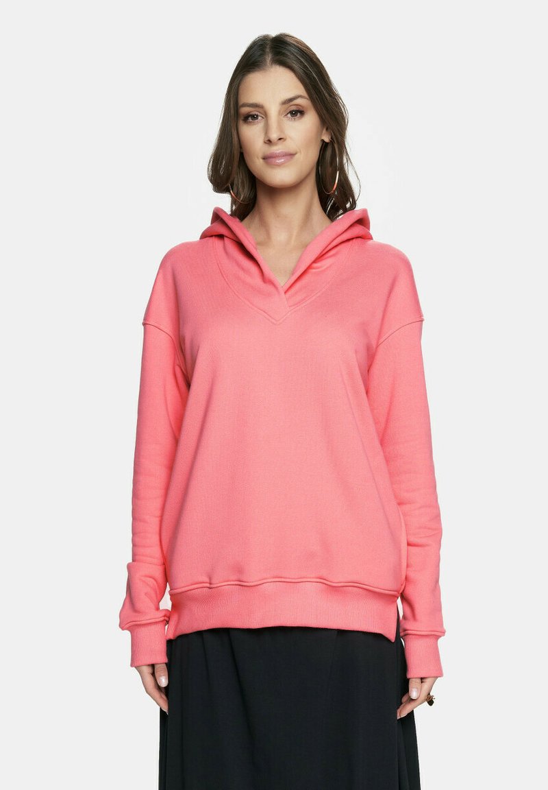 Korale różowa bluza z kapturem o kroju w serek, luźnym fasonie, ściągaczami na rękawach i na dole. Miękka faktura, minimalne zdobienia i swobodna sylwetka.