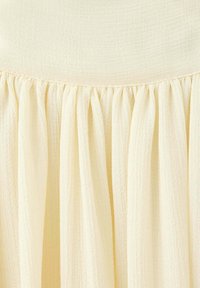Gros plan d’un tissu jaune pâle froncé avec des plis lâches et texturés créant une apparence douce et fluide.