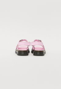 Rosa to-strap sandaler med en svart teksturert såle. Har justerbare stropper og gule sømdetaljer. Designet for komfort og støtte.