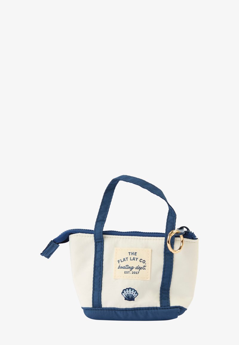 Petit sac cabas blanc et marine avec anses courtes, fermeture zippée, anneau doré, logo brodé et motif coquillage à l’avant.