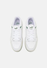 Baskets Slipstream blanches de Puma avec des accents verts, lacets attachés, vues du dessus sur un fond blanc uni.