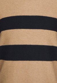 Tissu tricoté à rayures horizontales beige et noir avec un motif texturé et des coutures visibles le long des bords des rayures.