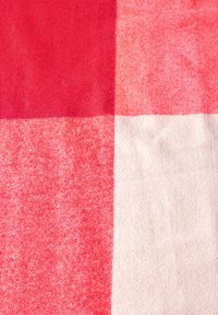 Tissu à carreaux rouge et rose pâle, texture douce avec un tissage visible. Des carrés de différentes tailles créent un motif contrasté.