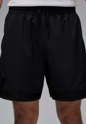Schwarze Sportshorts mit elastischem Bund und Kordelzug, getragen von einer Person vor einem schlichten Hintergrund.