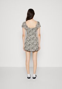 Kleid mit Blumenmuster, kurzen Puffärmeln, quadratischem Rückenteil und geraffter Taille. Schwarz-weiße Farbgebung; überknielange Länge.