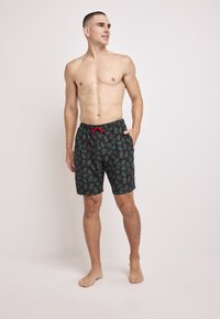 Herrbadshorts i mörkgrön färg med ett tropiskt bladmönster i blå och röda accenter, elastisk midja med snörning.
