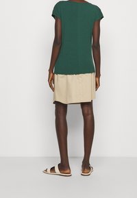 Groen, kort mouwen top gemaakt van zachte stof, gecombineerd met een beige rok. De top heeft een ronde halslijn en een comfortabele pasvorm, met minimale details.