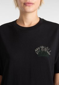 Black cotton T-shirt with a crew neck, featuring a green and gray graphic logo on the left chest, textured with a distressed appearance.