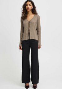 Béžový žebrovaný cardigan s V-čkem a zavazováním, kombinovaný s černými širokými kalhotami s vysokým pasem. Jednoduchý, přiléhavý design, uvolněná textura.