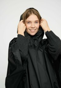 Mustat vedenpitävät ponchot, jossa on etuvetoketju, huppu ja ribbaus harmaa villatakki hihassa. Tasainen rakenne kiiltävällä pinnalla.