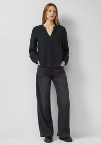 Schwarze langärmelige Bluse mit V-Ausschnitt, kombiniert mit lockeren dunkelgrauen Jeans, die eine lässige Passform und eine glatte Stoffstruktur betonen.