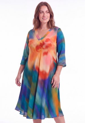 Vrouw draagt een kleurrijke, vloeiende knielange jurk met driekwart mouwen en een V-hals, met een levendig abstract patroon in oranje, blauw en groen.