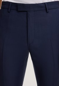 Marineblaue maßgeschneiderte Hose aus strukturiertem Stoff mit einem dezenten Rautenmuster, flachem Frontdesign und Taschen.