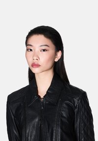 Giubbotto di pelle nera con dettagli trapuntati sulle spalle e chiusura a zip. Il materiale ha una finitura leggermente testurizzata con un colletto strutturato.