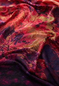 Bunt gemustertes Gewebe mit lebhaften Blumenmustern in Rot-, Violett- und Goldtönen, das eine weiche, fließende Textur aufweist.