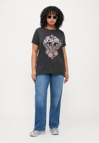 T-shirt gris foncé avec un motif "Rock and Roll" mettant en avant un design ailé et des fleurs, associé à un jean bleu clair et des baskets grises.