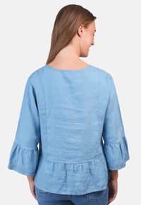 Helles blaues Leinenoberteil mit dreiviertellangen Glockenärmeln und gewelltem Saum. Verfügt über einen weiten runden Ausschnitt und dezente Stickdetails.