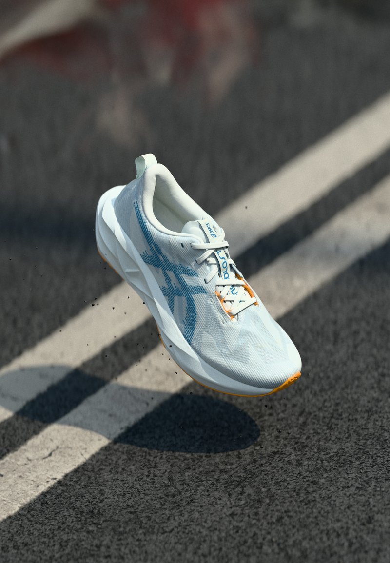 White athletic shoe with a textured upper featuring light blue accents, orange outsole, and a reinforced heel tab; illustrated laces.