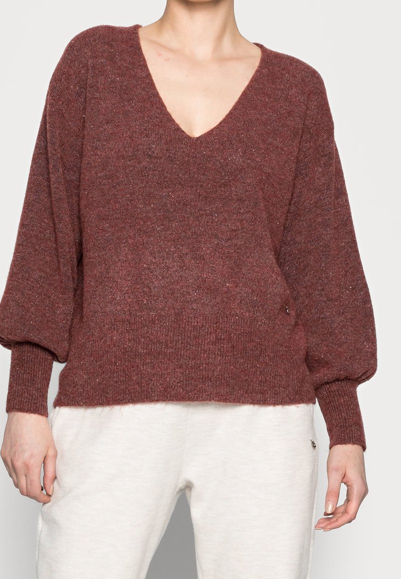 Pull en maille bordeaux avec un décolleté en V profond et des manches bouffantes amples. Doté de poignets et d'un ourlet côtelés, d'une texture douce et d'une coupe décontractée.