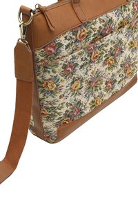 Sac à motif floral avec des accents en cuir marron, présentant une texture tissée et une bandoulière réglable, conçu avec une fermeture éclair et une poche avant.
