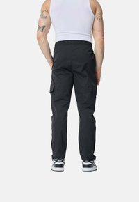 Pantalons cargo noirs avec une taille élastique, des poches latérales et une coupe ample, assortis à des baskets noir et blanc.