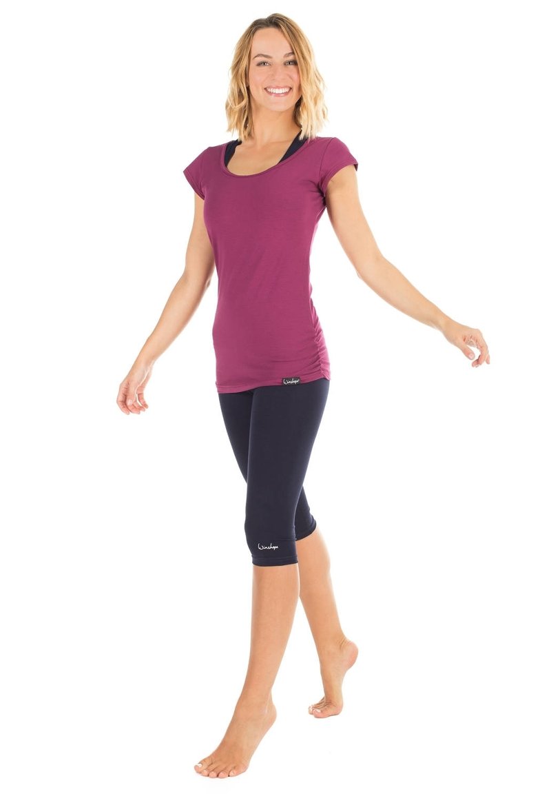 Enganliegendes lila Sportoberteil mit kurzen Ärmeln, kombiniert mit knielangen marineblauen Leggings. Glatter Stoff und dezentes Markenlogo-Detail.