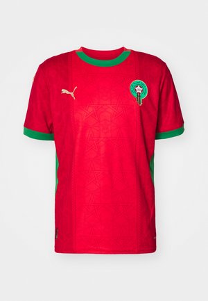 Rød fotballdrakt med kort erme og grønne detaljer, med et teksturert mønster av stjerner, Puma-logoen og et sirkulært marokkansk emblem på brystet.