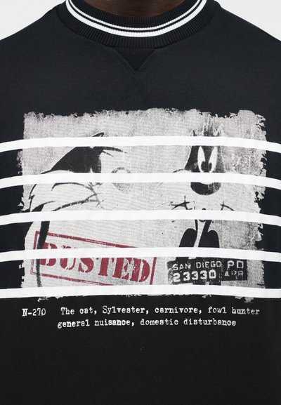 Sweat-shirt noir avec une photo d'identité détériorée du chat dessin animé Sylvester, estampillée "Arrêté", avec un texte le décrivant comme une nuisance et un chasseur de volaille.