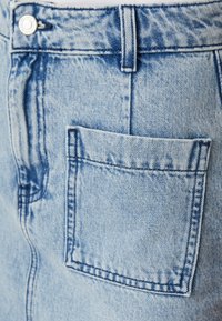 Șorturi din denim de nuanță albastru deschis, cu un buzunar la spate, cusături contrastante și un sistem de închidere cu un buton metalic la talie, având o textură decolorată.