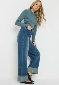 Stickad polotröja i dämpad teal, kombinerad med vida blå denimjeans med uppvikt fåll. Svarta ballerinaskor fulländar looken.