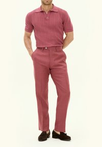 Polo in un rosa chiaro testurizzato, con colletto e bottoni, abbinato a pantaloni beige chiaro su misura e mocassini marroni.